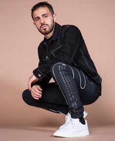 a man sitting on the ground with his legs crossed and looking at the camera while wearing black