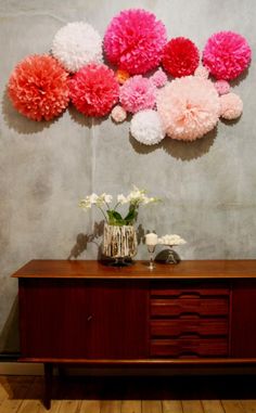 there are many pom poms hanging on the wall above a wooden table with vases and flowers