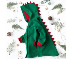 "A green baby dinosaur jacket is a great handmade gift for girls and boys.  The warm stegosaurus coat is suitable for walks on the street in spring or autumn. The kid's spring overcoat is made of fleece knitted fabric, which perfectly warms. The lining is made of jersey fabric.  In the front, there are two pockets for small treasures. The buttoned jacket is comfortable to wear for both parents and children. The soft toddler coat looks very fun and attractive. Contrasting spikes are fun and eye-catching.  The jacket is fully lined. The color of the lining matches the color of the spikes (red).  You can change the color of the lining by writing me a letter. I'll pick it up for you. Choose your dinosaur costume color.  It is hipster baby clothes. In the photo is my little Stephanie (purple di Playful Green Winter Outerwear, Playful Green Outerwear For Fall, Playful Green Long Sleeve Outerwear, Dinosaur Jacket, Costume Dinosaure, Rex Costume, T Rex Costume, Hipster Baby Clothes, Toddler Coat