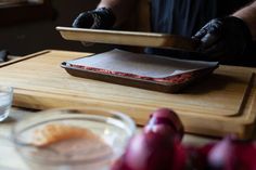 a person in black gloves cutting meat on a wooden board