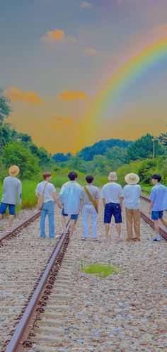 a group of men standing on train tracks with a rainbow in the background