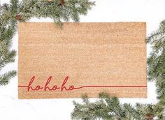 a door mat with the word hoho written on it next to evergreen branches and pine cones