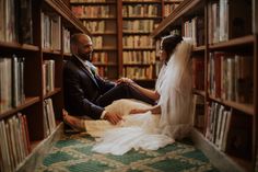 a bride and groom sitting on the floor in front of bookshelves