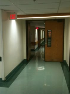 an empty hospital hallway with the exit sign lit up