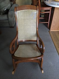 a wooden chair with wicker seat and back rests on carpeted floor next to couch