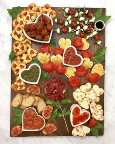 heart shaped appetizers are arranged on a cutting board with leaves and toppings