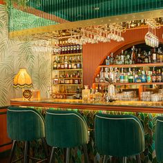 a bar with green velvet chairs and gold chandelier hanging from it's ceiling