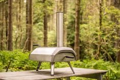 an outdoor pizza oven sitting on top of a picnic table in the woods with trees behind it