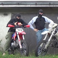 two men standing next to each other on dirt bikes