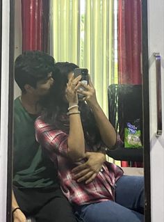 a man and woman taking a selfie in front of a mirror with red curtains