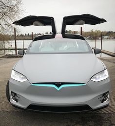 an electric car with its doors open in a parking lot next to the water and trees