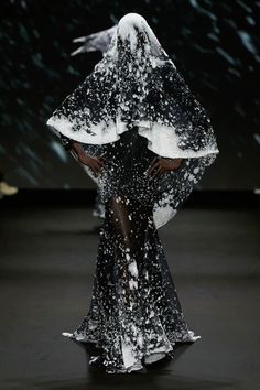 a woman in a black and white dress with snow on her head is walking down the runway