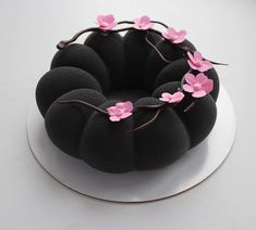 a black cake with pink flowers on top sitting on a white plate and ready to be eaten