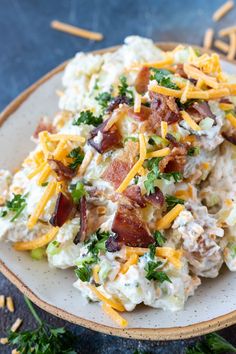 a white plate topped with potato salad covered in bacon and cheddar cheeses