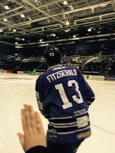 a hockey player standing on the ice with his hands up in front of him as he claps