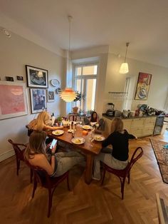 three women sitting at a table with plates of food in front of them, while one woman is on her cell phone