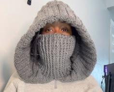 a woman wearing a gray knitted hoodie covering her face