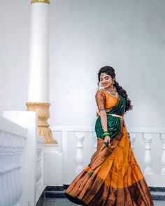 a woman in an orange and green sari is standing on the steps with her hands behind her back