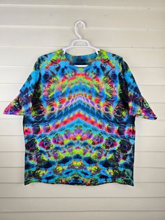 a t - shirt hanging on a white wall with a tie dye pattern in the middle