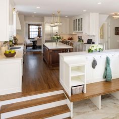 an open kitchen with white cabinets and wood flooring, along with stairs leading up to the dining room