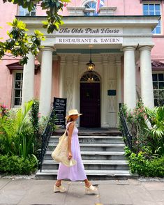 a woman walking in front of the old pink house restaurant and tavern, with flags flying overhead