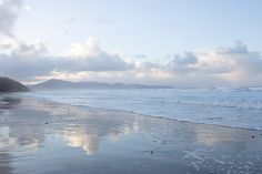 a beach with waves coming in to the shore and mountains in the distance on a cloudy day