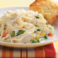 a white plate topped with pasta and veggies next to a piece of bread