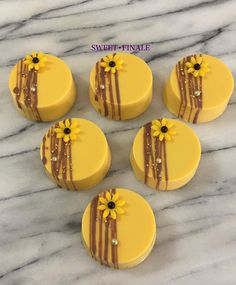 six yellow and brown decorated cookies sitting on top of a marble counter with chocolate drizzle