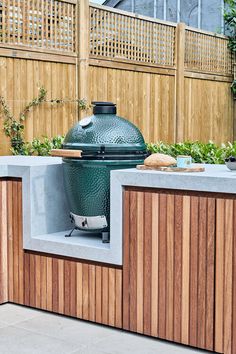 an outdoor grill is built into the side of a wooden fenced in area with potted plants