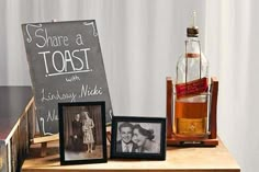 there is a bottle and two framed photos on the table next to each other with a chalkboard sign that says share a toast