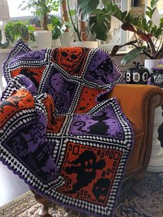 an orange and purple blanket sitting on top of a chair next to a potted plant