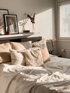 a bed with white sheets and pillows in a bedroom next to a window covered by blinds