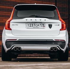 the back end of a white car parked in front of a brick building