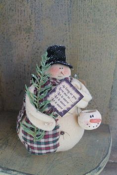 a small snowman holding a sign on the back of a chair with a tree in it