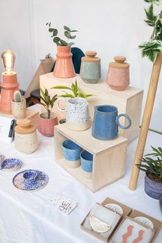 various vases and plates on display at an art show or sale with plants in the background