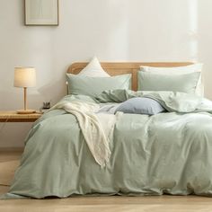 an unmade bed with light green sheets and pillows on top of it in a white room