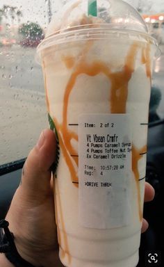 a person holding up a drink in front of a car window on a rainy day