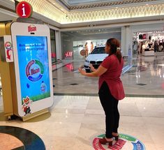 a woman is standing in front of a digital screen at the mall and looking at her cell phone