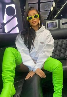 a woman sitting on top of a black chair wearing neon green pants and yellow sunglasses