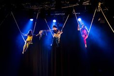 three women are performing aerial acrobatic tricks on stage with lights behind them