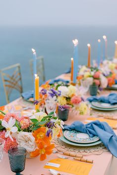 a long table with flowers and candles is set for an outdoor dinner by the ocean