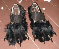 two pairs of shoes with black fur and claws on them sitting on a wooden floor