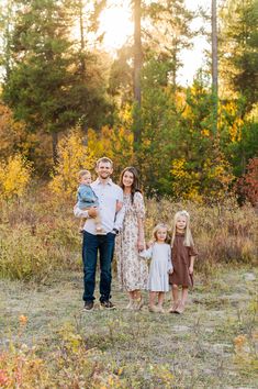 a family standing in the middle of a field with trees and bushes behind them at sunset