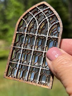 a hand holding a small piece of stained glass in front of a green field and trees