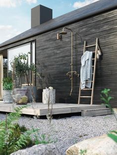 an outdoor shower is shown in front of a wooden building with plants and rocks on the ground