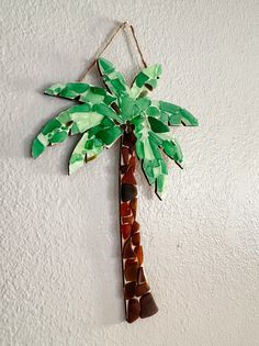 a paper palm tree hanging on the wall with green leaves and brown stones in it