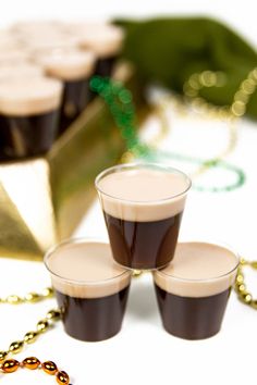 three shot glasses sitting on top of a table next to gold chains and green leaves