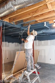 a man standing on a ladder in an unfinished room with exposed pipes and duct tape hanging from the ceiling