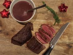 a wooden cutting board topped with meat next to a knife and bowl filled with sauce