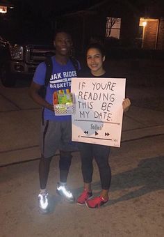 two people holding up a sign that says if you're reading this be my date